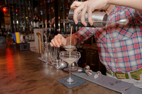 Bartender is straining drink in glass