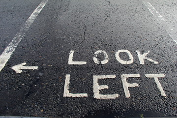 Sign instructing pedestrians to look left,painted on busy street