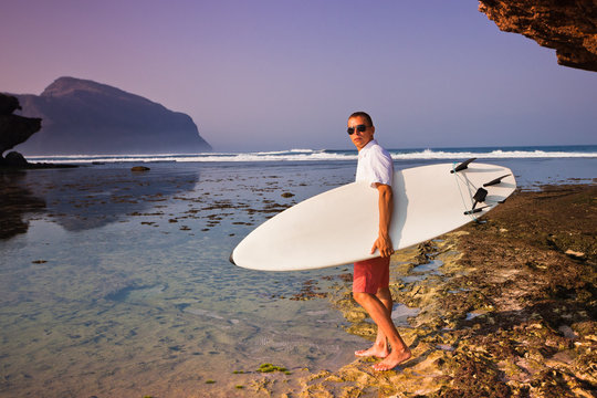 Man surfer with surfboard on a coastline. Bali. Indonesia