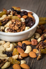 Assorted nuts in white bowl on wooden background.
