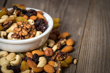 Assorted nuts in white bowl on wooden table.