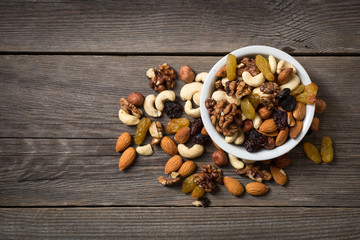 Assorted nuts in white bowl on wooden surface.