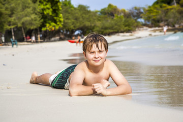 boy lies at the sandy beach and enjoys the fine warm sand