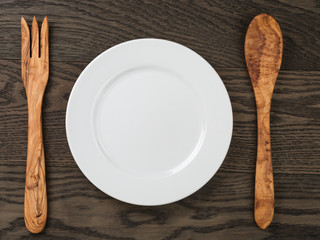 empty white plate with wood fork and spoon on oak table