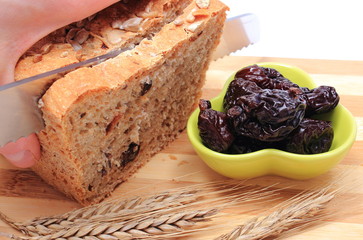Slicing fresh bread, dried plums and ears of wheat