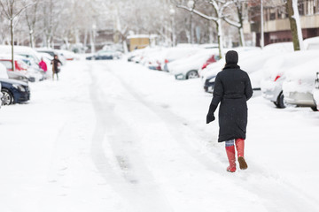 Woman dressed in black coat and boots walking alone on the snow