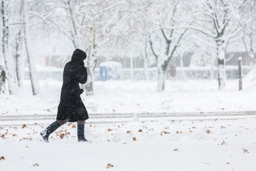 Fototapeta premium Woman dressed in black coat walking alone during heavy snowstorm