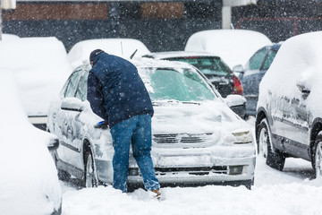 Man scraping frozen snow from the car windows during snowfall
