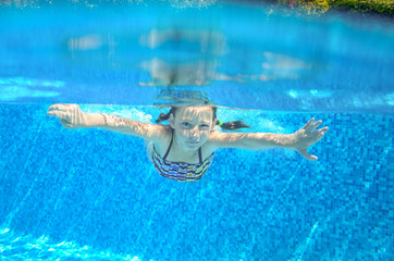 Fototapeta na wymiar Kid swims in pool underwater, girl swimming and having fun