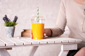 Female hand at wooden table with fast food closed cup of orange