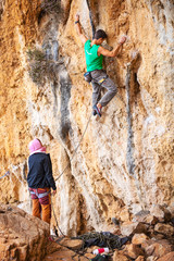 Young man lead climbing on cliff, female climber belaying