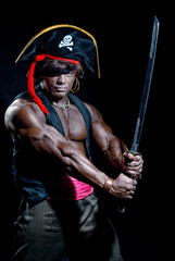Fototapeta na wymiar Muscular black man in a pirate hat and sword on a black backgrou
