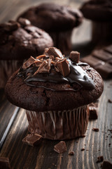 Chocolate muffins with icing and chocolate pieces. Dark lighting
