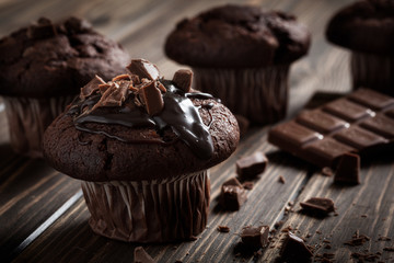 Chocolate muffins with icing and chocolate pieces. Dark lighting