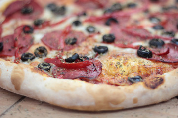 Closeup of pizza with salami, peperoni, black olives and pepper.