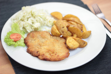 Wiener schnitzel with fried potato wedges and cabbage salad.