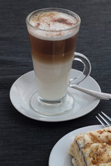 Closeup of cafe latte sprinkled with cocoa and piece of cake.
