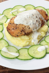 Closeup of roasted piece of chicken on mashed potatoes.