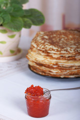 Банка красной икры на фоне большой стопки блинов на столе