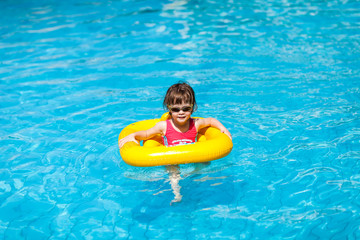 Cute girl swims in a pool in a yellow life preserver