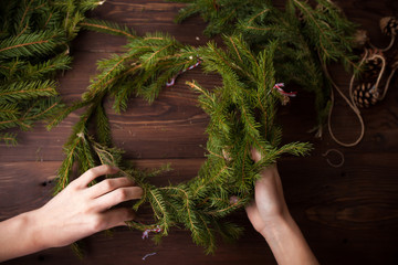 Making Christmas wreath with hands on wooden background