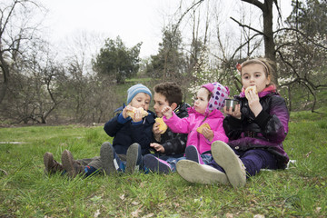 Naklejka na ściany i meble Kids on spring meadow sit on the grass and eat cookies.