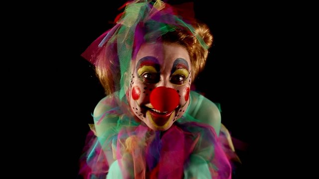female clown is making grimaces in front of  black background