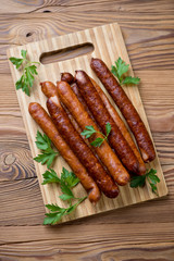 Wooden chopping board with smoked sausages, above view