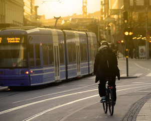 Bike commuter and tram in sunlit city - obrazy, fototapety, plakaty