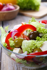 Greek salad in glass dish on wooden table background
