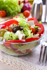Greek salad in glass dish with fork and vegetables background