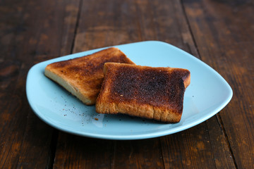 Burnt toast bread on turquoise plate, on wooden table