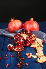 Juicy ripe pomegranates on wooden table, on dark background