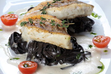 Auf der Haut gebratene Fischfilets auf schwarzen Bandnudeln mit Soßenschäumchen