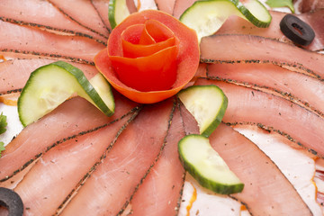A dish of sliced meat decorated with olives, cucumbers, parsley
