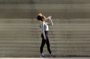 Fototapeta na wymiar African american sports woman drinking from water bottle