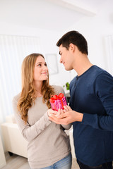 young couple man woman at home offering gifts for lover's day