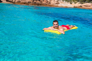 Happy man relaxing on inflatable mattress in clear sea