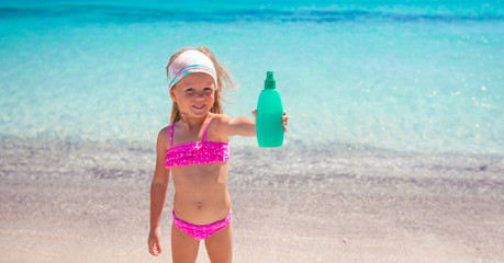 Little adorable girl in swimsuit with suntan lotion bottle