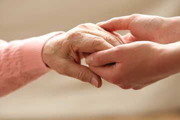 Old and young holding hands on light background, closeup