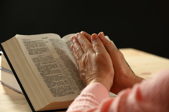 Hands of old woman with Bible on table and dark background