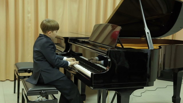 Boy playing the grand piano in the hall of the music school