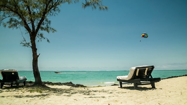 Beach lounge chairs and paraglider in tropical horizon 