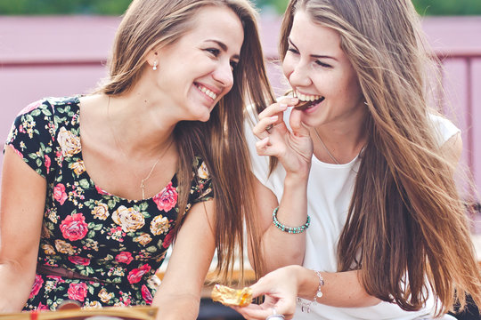 Two young females talk and laugh while eating chocolates outdoor