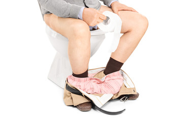 Studio shot of the legs of a man sitting on a toilet