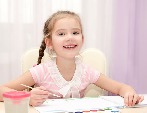 Cute smiling little girl drawing with paint and paintbrush
