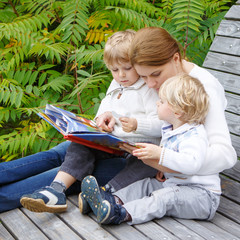 woman and two little siblings sitting on bench in park and readi