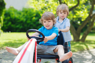 Two funny little boys having fun with race car outdoors