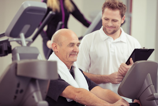 freundlicher trainer unterstützt senior im fitness-studio