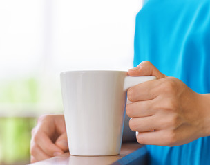 Fototapeta na wymiar Young woman in blue dress enjoying a mug of beverage